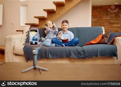 Children bloggers sitting on sofa at camera, little vloggers. Kids blogging in home studio, social media for young audience, online internet broadcast. Children bloggers sitting on sofa at camera