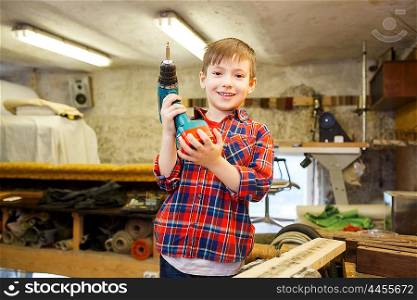 children, carpentry, profession and people concept - happy little boy with drill at workshop