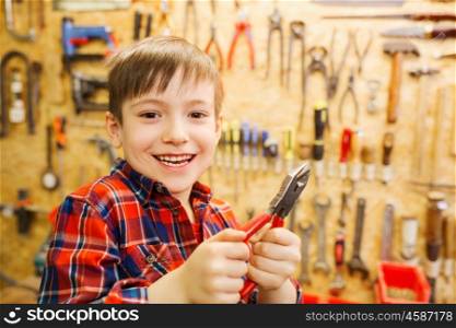 children, carpentry, profession and people concept - happy little boy with pliers at workshop