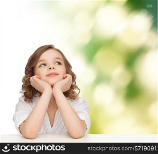 children, childhood, ecology and happy people concept - beautiful girl sitting at table, looking up and dreaming over green background