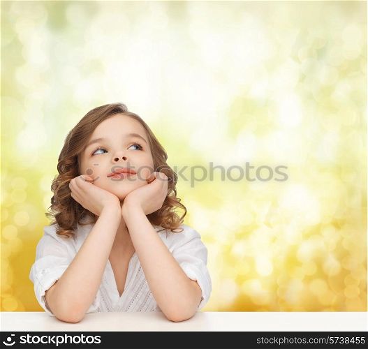 children, childhood, holidays and happy people concept - beautiful girl sitting at table, looking up and dreaming over yellow lights background