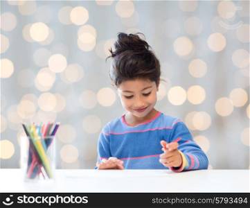 children, creativity and happy people concept - happy little girl drawing with coloring pencils over holidays lights background