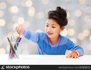 children, creativity and happy people concept - happy little girl drawing with coloring pencils over holidays lights background