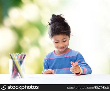 children, creativity and happy people concept - happy little girl drawing with coloring pencils over green background