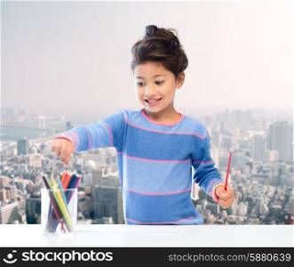 children, creativity and happy people concept - happy little girl drawing with coloring pencils over city background