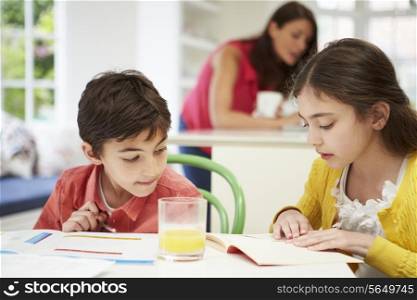 Children Doing Homework As Mother uses Laptop In Background