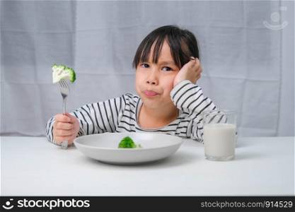 Children don&rsquo;t like to eat vegetables. Cute Asian girl refusing to eat healthy vegetables. Nutrition and healthy eating habits for children.