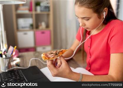 children, education and distant learning concept - close up of teenage student girl in earphones with laptop computer eating pizza and writing to notebook at home. student girl in earphones eating pizza at home