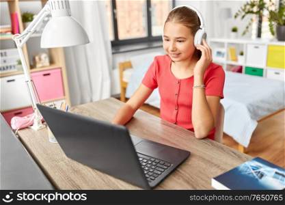 children, education and distant learning concept - happy smiling teenage student girl in headphones with laptop computer at home. girl in headphones with laptop computer at home