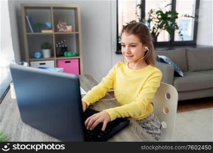 children, education and distant learning concept - little student girl in earphones with laptop computer at home. girl in earphones with laptop computer at home