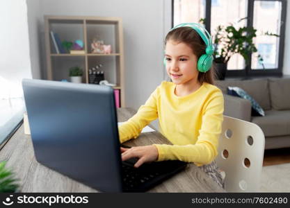 children, education and distant learning concept - little student girl in headphones with laptop computer at home. girl in headphones with laptop computer at home