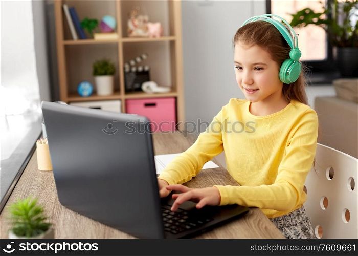 children, education and distant learning concept - little student girl in headphones with laptop computer at home. girl in headphones with laptop computer at home