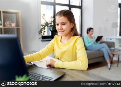 children, education and distant learning concept - smiling student girl with laptop computer and notebook and mother with tablet pc at home. student girl with laptop learning online at home