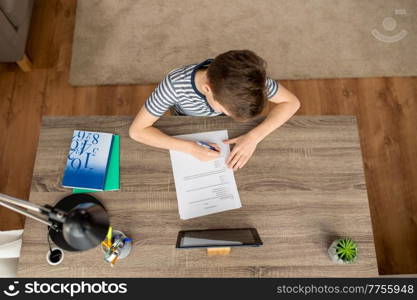 children, education and distant learning concept - student boy with tablet pc computer and books on table doing school test at home. student boy doing school test at home
