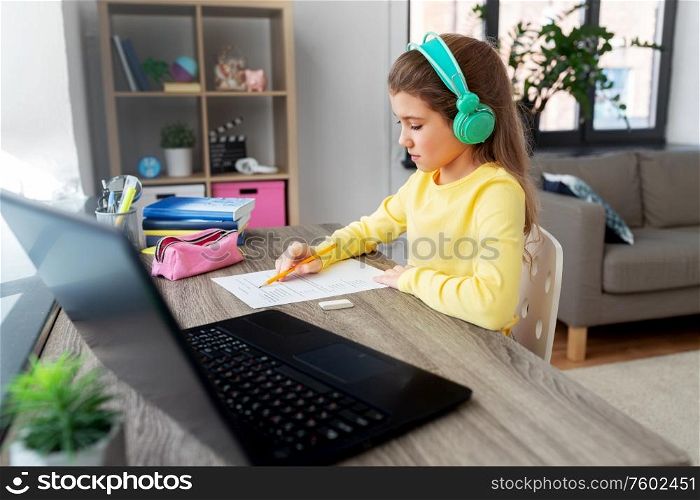 children, education and distant learning concept - student girl in headphones doing school test at home. student girl doing school test at home