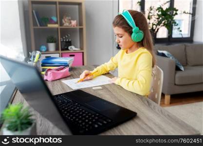 children, education and distant learning concept - student girl in headphones doing school test at home. student girl doing school test at home