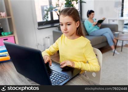 children, education and distant learning concept - student girl with laptop computer and mother reading book at home. student girl with laptop learning online at home