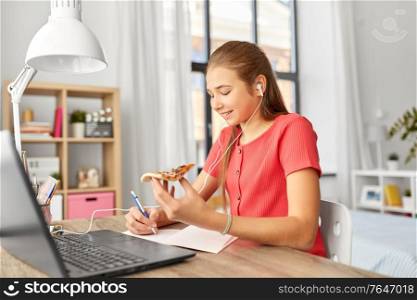 children, education and distant learning concept - teenage student girl in earphones with laptop computer and pizza writing to notebook at home. student girl in earphones with pizza at home