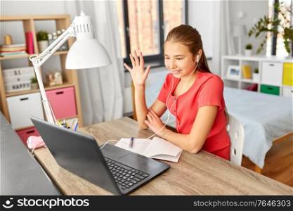 children, education and e-learning concept - happy smiling teenage student girl in earphones with laptop computer having video call at home. student girl with laptop having video call at home