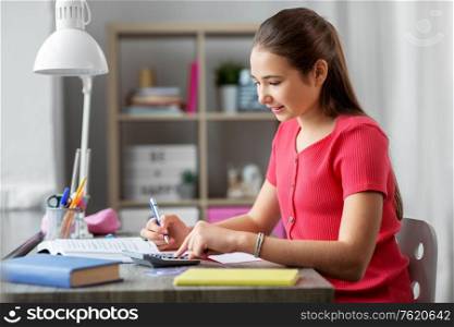children, education and learning concept - happy smiling teenage student girl counting on calculator at home. student girl counting on calculator at home