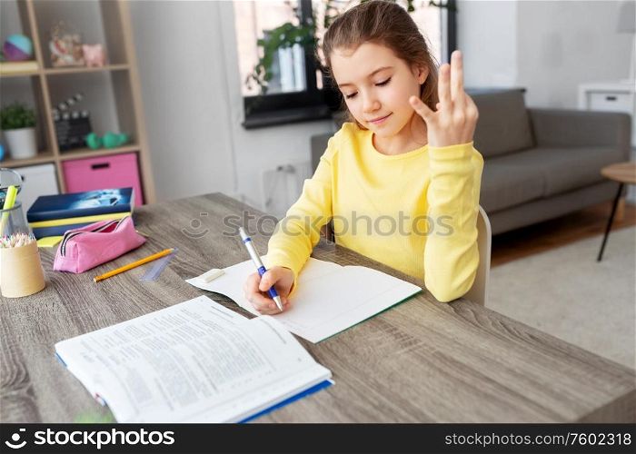 children, education and learning concept - happy student girl with book counting fingers and writing to notebook at home. student girl with book writing to notebook at home