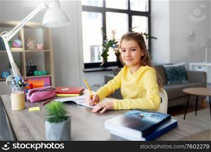 children, education and learning concept - happy student girl with book writing to notebook at home. student girl with book writing to notebook at home