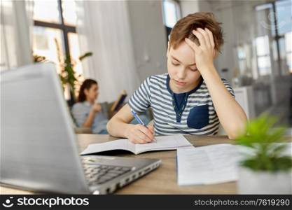 children, education and learning concept - student boy with book writing to notebook at home. student boy with book writing to notebook at home
