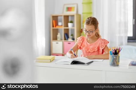 children, education and learning concept - student girl with book writing to notebook at home. student girl with book writing to notebook at home