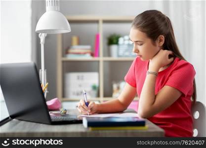 children, education and learning concept - teenage student girl with laptop computer writing to notebook at home. teenage student girl writing to notebook at home
