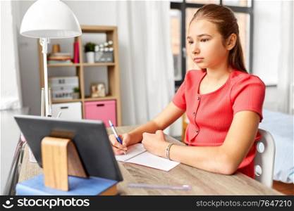 children, education and learning concept - teenage student girl with tablet pc computer writing to notebook at home. student girl with tablet pc learning at home
