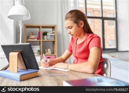 children, education and learning concept - teenage student girl with tablet pc computer writing to notebook at home. student girl with tablet pc learning at home