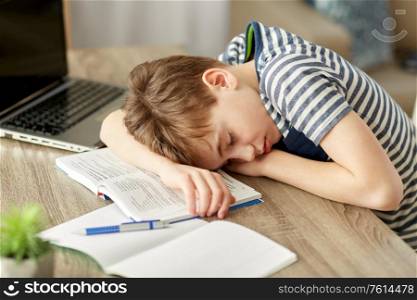 children, education and learning concept - tired student boy sleeping on desk at home. tired student boy sleeping on desk at home