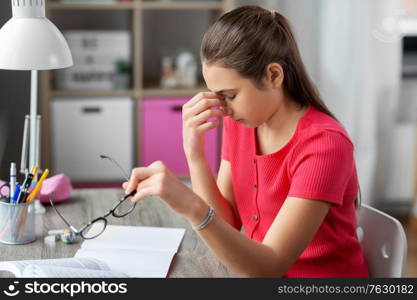 children, education and learning concept - tired teenage student girl with glasses rubbing her eyes at home. tired teenage student girl with glasses at home