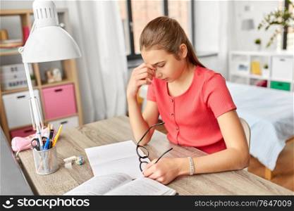 children, education and learning concept - tired teenage student girl with glasses rubbing her eyes at home. tired teenage student girl with glasses at home