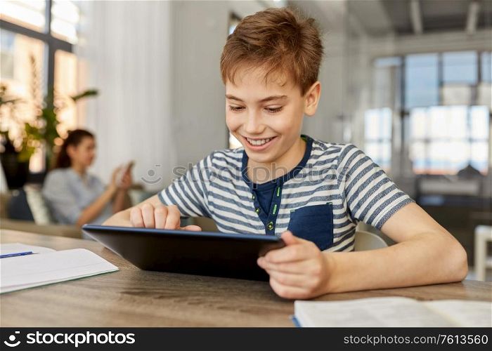 children, education and school concept - happy student boy with tablet pc computer learning at home. student boy with tablet computer learning at home