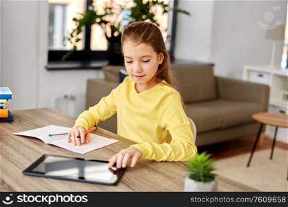 children, education and school concept - happy student girl with tablet pc computer writing to notebook at home. student girl writing to notebook at home