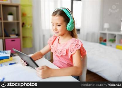 children, education and technology concept - happy student girl in headphones with tablet computer at home desk. girl in headphones with tablet computer at home
