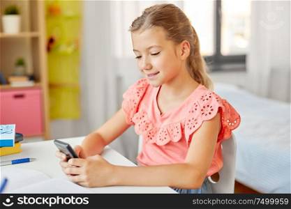 children, education and technology concept - happy student girl using smartphone at home. happy student girl using smartphone at home