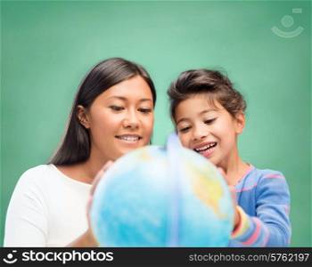 children, education, school and happy people concept - happy teacher and little schoolgirl with globe over green chalk board background