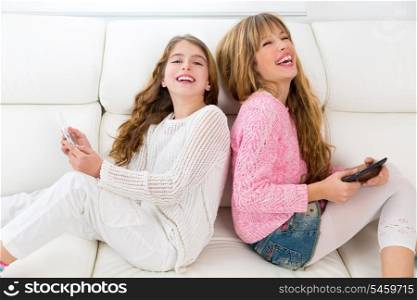 Children friends kid girls having fun playing back to back with tablet pc on white sofa