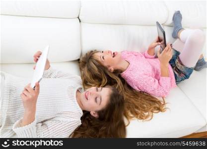 Children friends kid girls having fun playing with tablet pc lying on white sofa