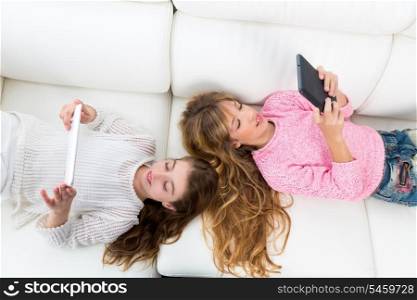 Children friends kid girls having fun playing with tablet pc lying on white sofa
