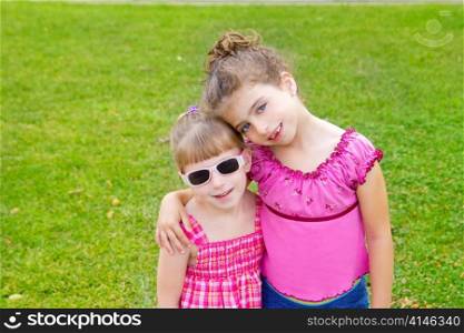 children girls hug in green grass park with pink dress