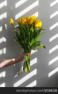 Children hand holding flowers over gray background. Bouquet of yellow tulips for Birthday, Happy mothers or Valentines day.. Children hand holding flowers over gray background. Bouquet of yellow tulips for Birthday