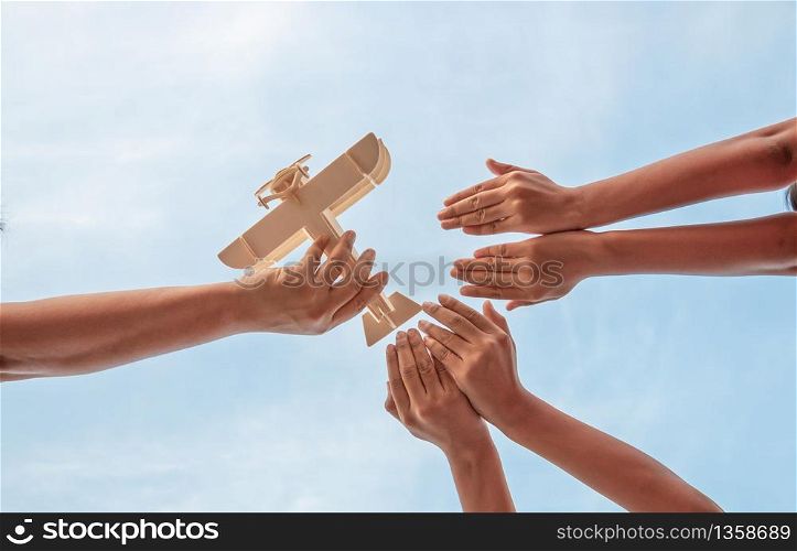 Children hands and father hands playing wooden plane toy on a beautiful sky background, Low angle view.