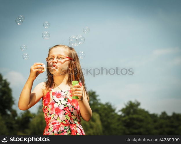 Children happiness and carefree concept. Little girl having fun blowing soap bubbles in park green blurred background