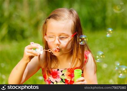 Children happiness and carefree concept. Little girl having fun blowing soap bubbles in park green blurred background