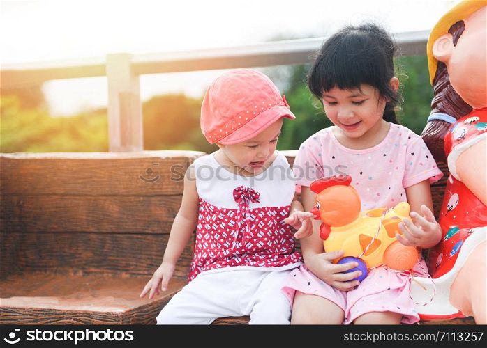 Children having fun playing outside Asian kids girl sitting on a bench happy with toys in the garden park / International Children?s Day