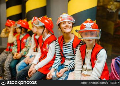 Children in helmets and uniform playing fireman, playroom indoor. Kids lerning firefighter profession. Boys and girls plays lifeguards, little heroes in equipment on playground