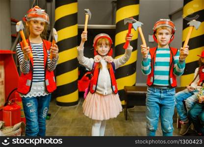 Children in helmets and uniform with tools in hands playing fireman, playroom indoor. Kids lerning profession. Boys and girls plays lifeguards, little heroes in equipment on playground
